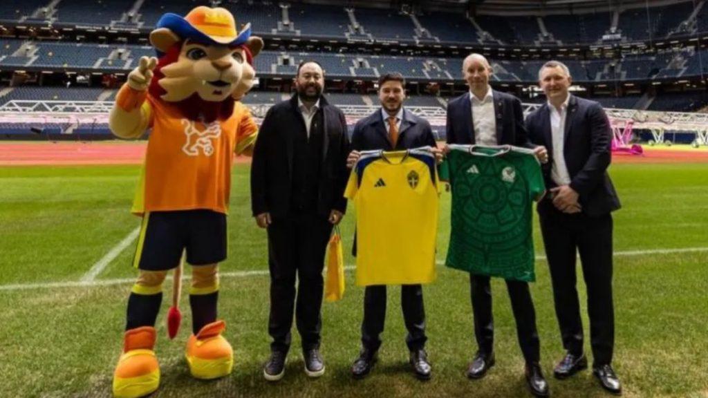 El-viaje-de-samuel-garcia-a-europa - La Razón Nl Mascot in Orange Outfit Posing with Four Men on a Soccer Field, Holding Yellow and Green Team Jerseys for Display at the Stadium. - La Razón Nl