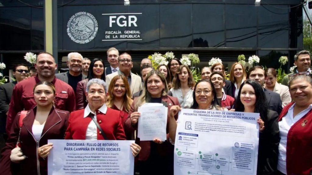 Group of Diverse Officials Posing in Front of a Black Fgr Building, Two People Holding Large Posters About Public Resources and Social Media Campaigns. - La Razón Nl