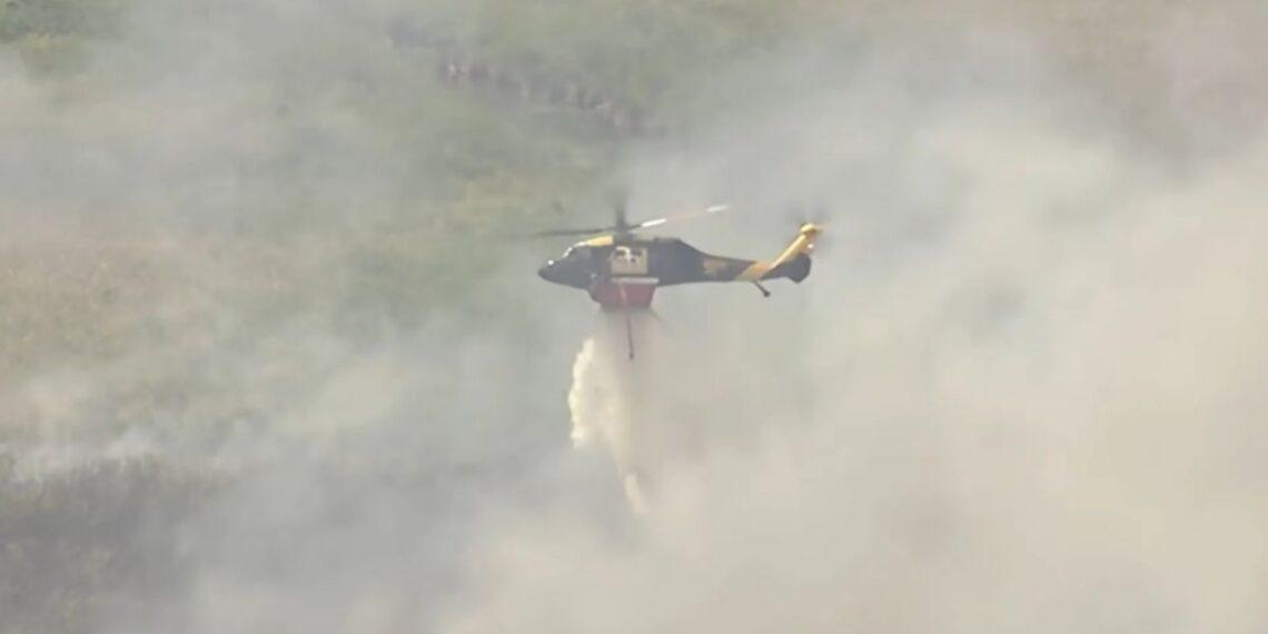 Firefighting Helicopter Releasing a Water Drop Amid Thick Smoke over a Hillslope. - La Razón Nl