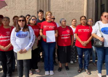 Group of Diverse Adults Standing Together Outside a Stone Building, Many Wearing Red Shirts That Read 'dónde Están?', Some in White Shirts with Blue Graphics, One Person Holding a Sheet of Paper. - La Razón Nl