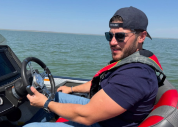 Man Wearing a Backward Cap and Sunglasses Steering a Motorboat on Calm Water Under a Clear Sky. - La Razón Nl