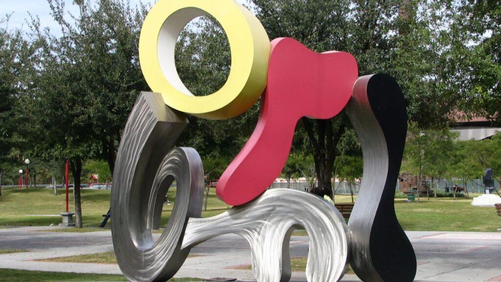 Abstract Metal Sculpture in a Park with Interlocking Yellow Ring, Pink Blob, Black Curve, and Silver Spirals Among Trees and Grass - La Razón Nl