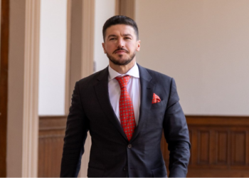 Man in a Dark Suit with a Red Tie and Pocket Square Standing in a Wood-paneled Hallway, Looking at the Camera. - La Razón Nl